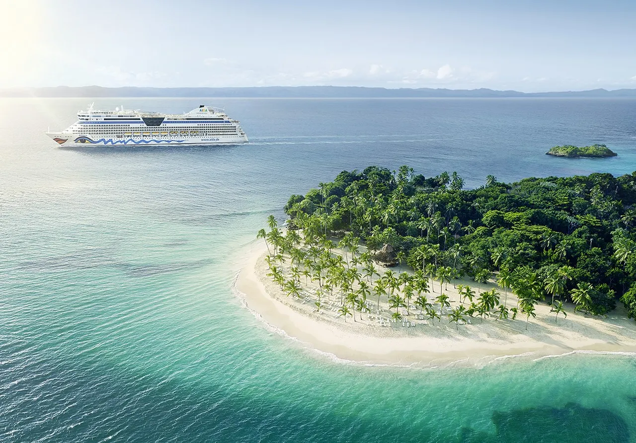 AIDAdiva kreuzt im türkisfarbenem Meer vor einer Karibikinsel mit Sandstrand