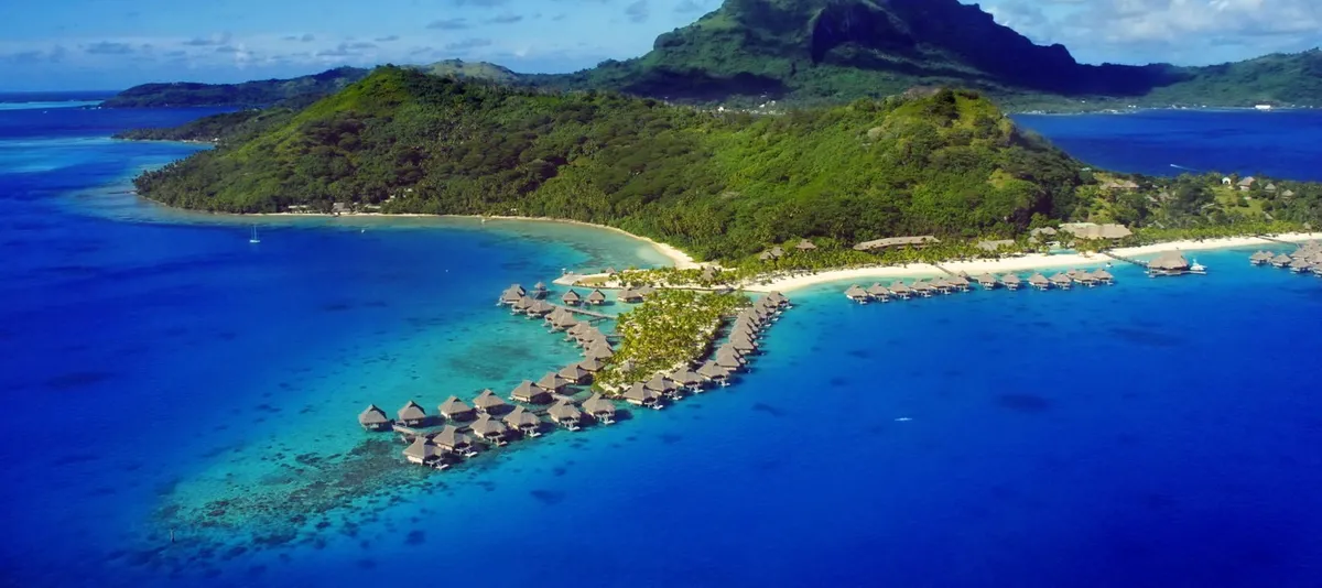 Bora Bora aus der Vogelperspektive mit grünen Küstenbergen und in allen Blautönen schimmerndem Meer