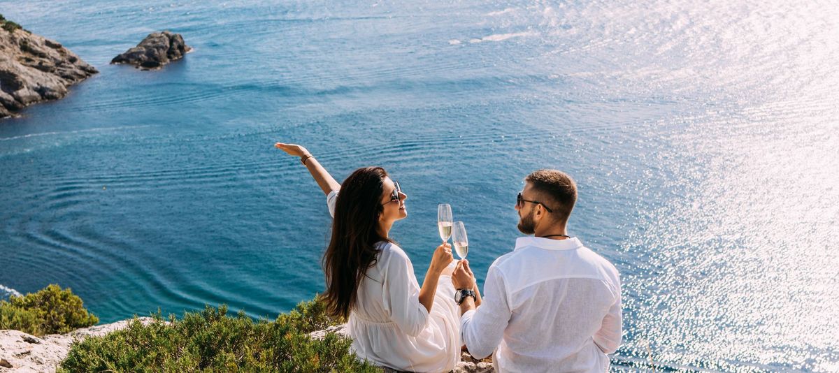 Paar auf den Cliffs stoßen mit Sektgläsern an und blicken auf das Meer
