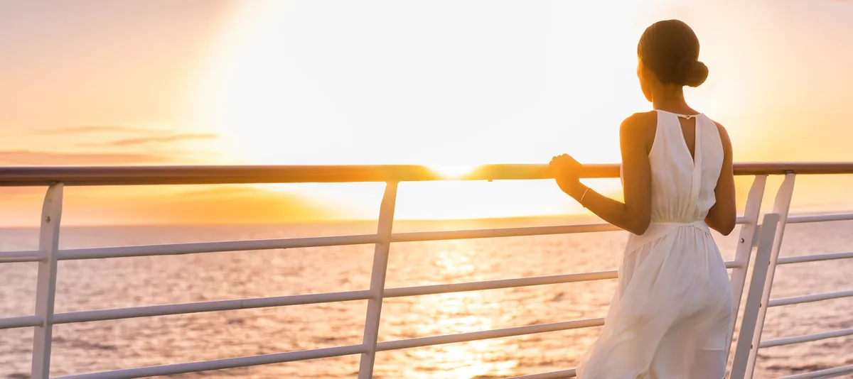 Frau steht an der Reling eines Schiffs und blickt auf das Meer