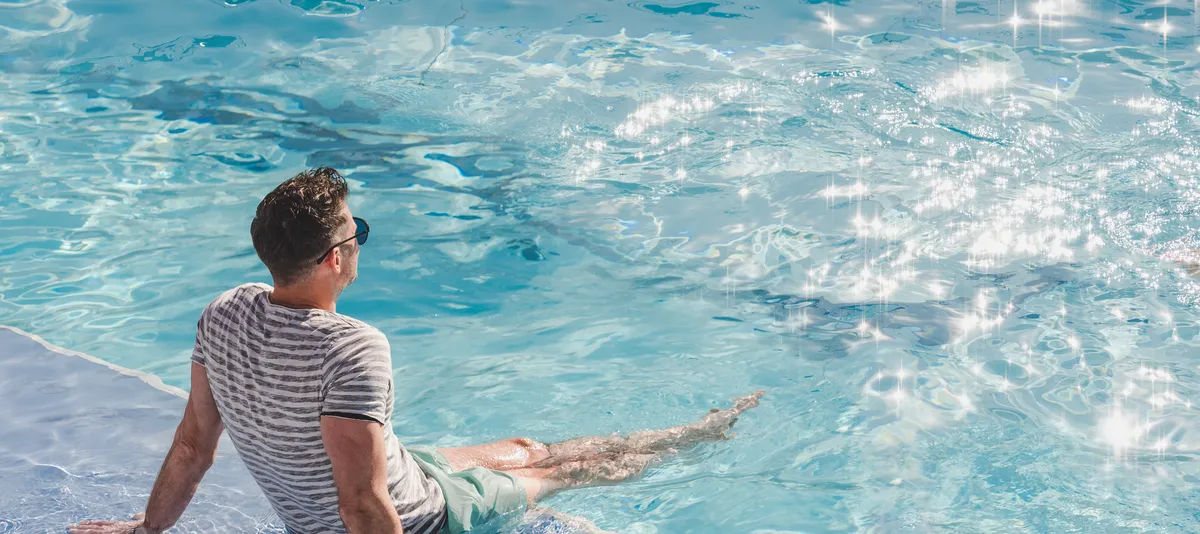 Mann sitzt in Kleidung am Pool