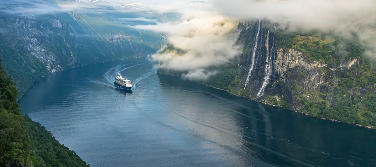 View on river surrounded by mountains, TUI Ship is driving towards viewer